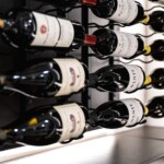 If you look closely, you can see this custom glass wine cellar's metal racking, attached to the backer boards. They're designed to showcase the bottles in a horizontal, label-forward position which makes it easier for anyone to read the label and grab a bottle.